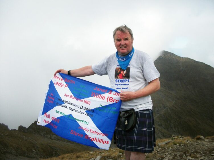 Jock Mcinnes on a mountainside with a Scottish flag.