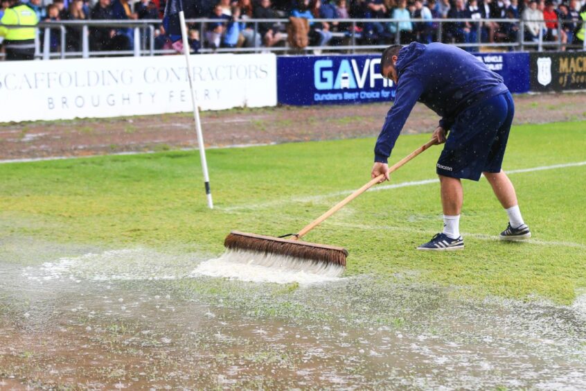 Dundee groundsman Brian Robertson sweeps rain from the Dens Park pitch in August. Image: David Young/Shutterstock