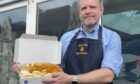 Gavin Murray of McKays Fish and Chip Shop holding a box containing fish and chips outside the shop.