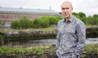 Image shows author Chris Brookmyre standing outdoors. Chris is standing with his hands in his pockets with a serious expression on his face.