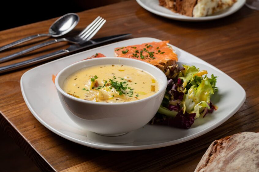 A bowl of Cullen Skink on a plate with a salmon sandwich and salad.