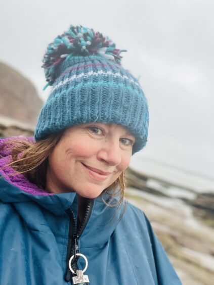 Jenny Paterson, founder of Wild Wimmin Swimmin, poses in a hat and dryrobe on the lochside. 