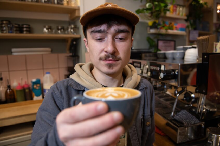 Lewis holding up a cup of coffee with a latte art heart on it.