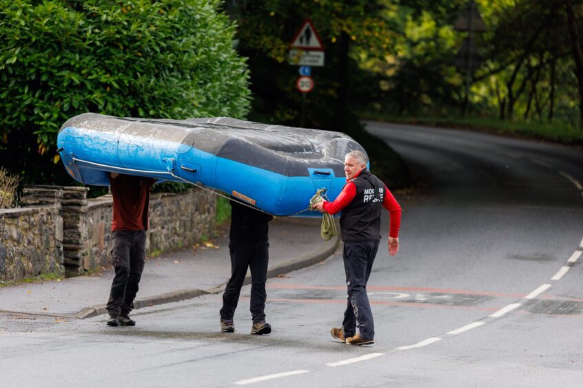 Three men walking across road at Strathtay carrying a canoe.