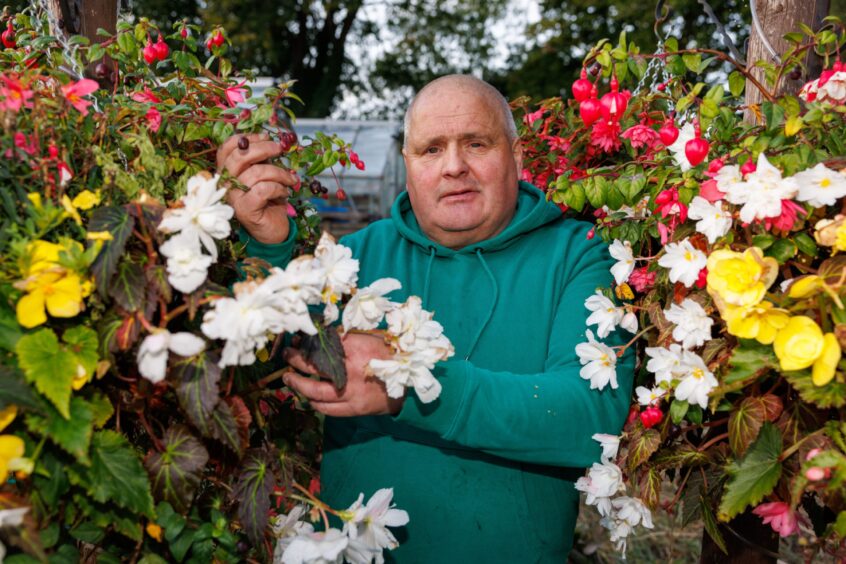 Kenny Orrock next to colourful hanging baskets of flowers at moncreiffe Island allotments