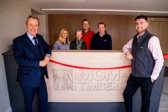 Staff of MGM Timber at new branch opening in St. Andrews. They are posing around the store sign with red ribbon draped across it.