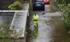 Person in high vis walking through deep water next to homes and cars at Perth's South Inch