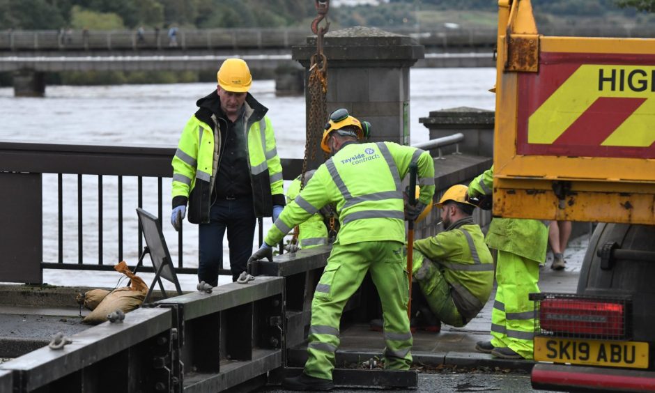 Council workers in yellow high vis gear installing heavy steel barriers on Queen's Bridge, Perth