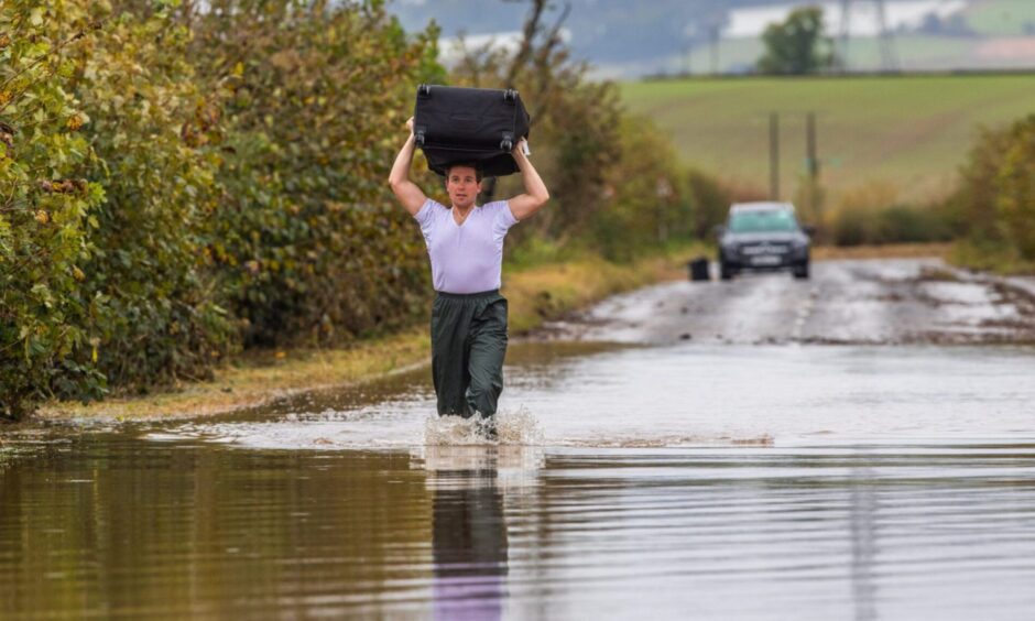 Scot Johnson wading through flood water with suitcase on shoulders