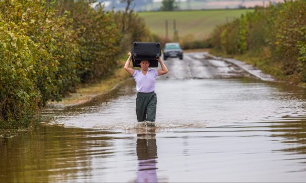 Scott Johnson walks through knee-deep flood water with suitcase on his shoulders on flooded road near Coupar Angus.