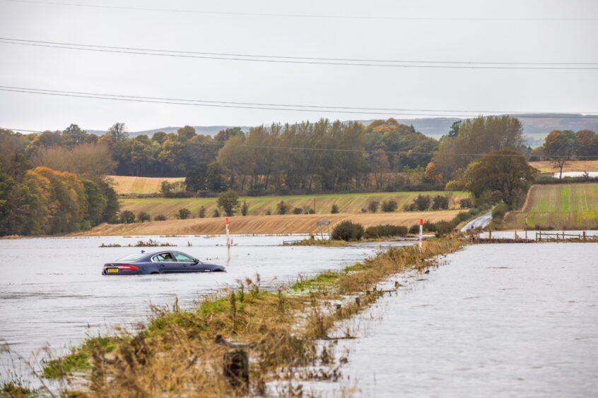 Stranded car in several feet of water in what looks like a lake with road from Meigle to Alyth in distance.