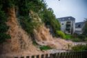 Filthy brown water pouring down slope into flooded Craigie Burn behind block of flats in Perth