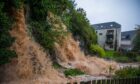 Filthy brown water pouring down slope into flooded Craigie Burn behind block of flats in Perth