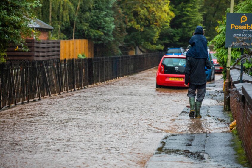 Man walking through flood water with small child on shoulders in Craigie area of Perth.