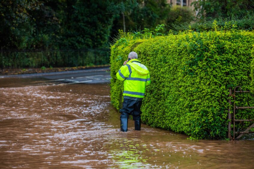 Man in high vis waterproofs standing in deep floodwater in Craigie area of Perth.