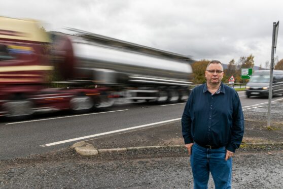 Fergus McCallum next to busy A9 at Pitlochry as blurred lorry and van go past