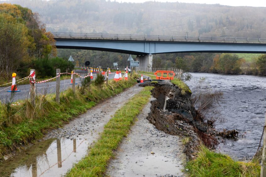 taped off section of roadway showing large chunk of embankment that has been washed away