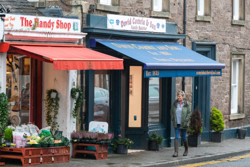 Person walking past Handy Shop and David Comrie and son family butcher in Comrie