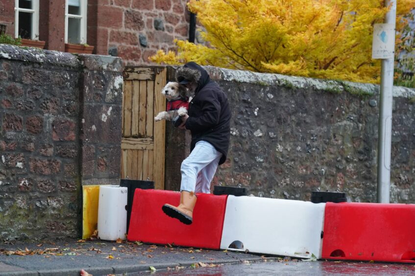 A man lifts his dog over a flood defence barrier erected on Church street in Edzell.