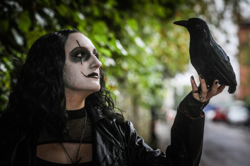 A woman dressed as the fantast character The Crow, holding a crow. 