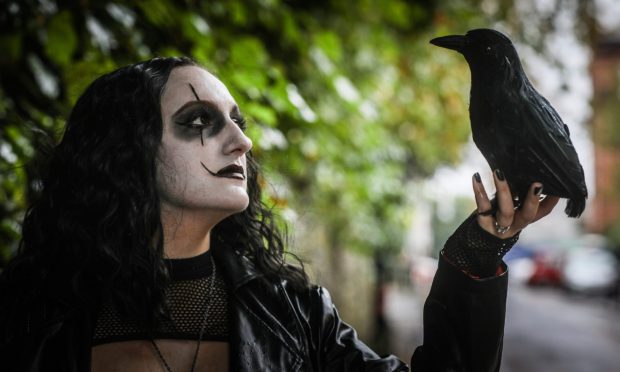 A woman dressed as the fantasy character The Crow, holding a crow.