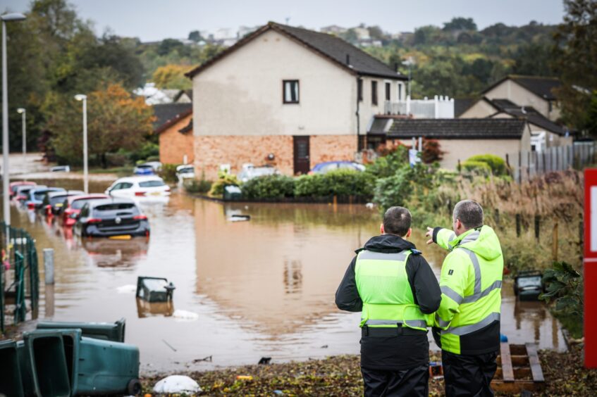 Men in yellow hi-vis gear pointing sat Invergowrie street with cars floating in deep flood water