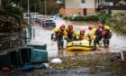 Flooded street in Invergowrie, with crew of rescue boat wading through water beside it