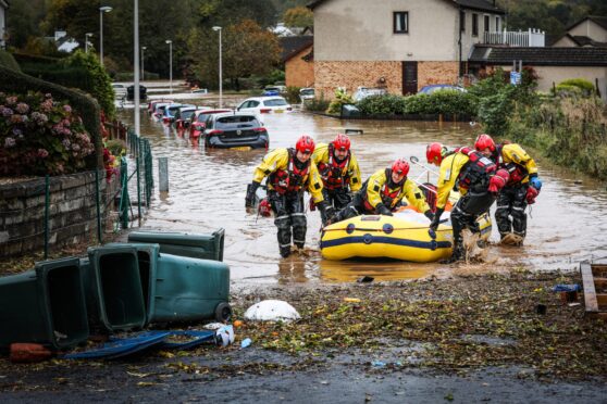 Flooded street in Invergowrie, with crew of rescue boat wading through water beside it