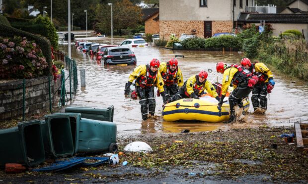 Flooded street in Invergowrie, with crew of rescue boat wading through water beside it