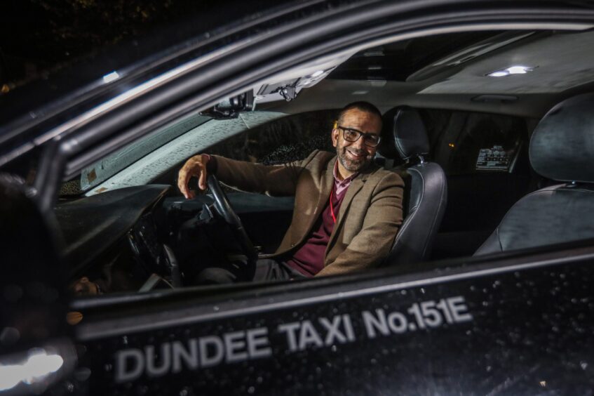 Driver Qaiser Habib smiling in his taxi. 