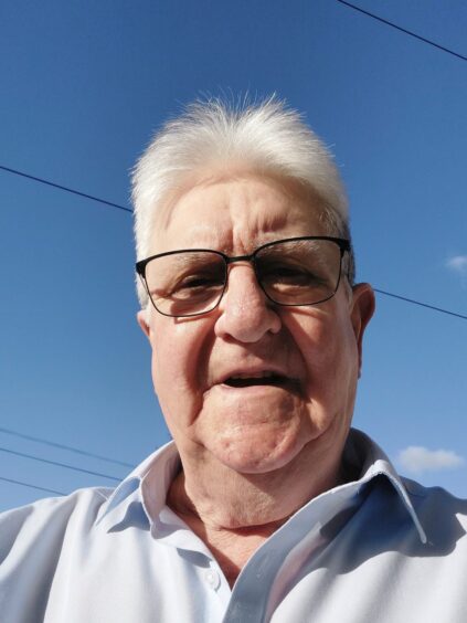 Eric Smith, wearing glasses and a white shirt, backed by a blue sky and power lines. 