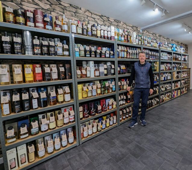 Steve McGilvray standing beside shelves full of bottles of whisky and other spirits in his shop in Perth