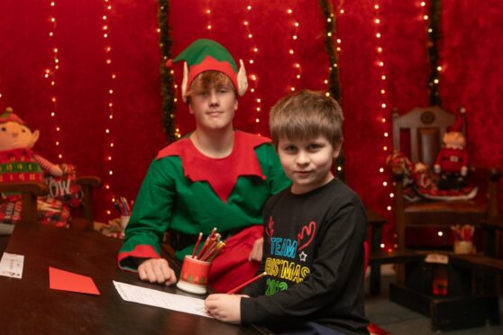 Luke Maher, 8, writing letter to Santa watched by a youth in elf costume at Santa's Post Office, Crieff.