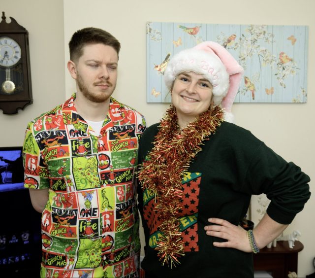 John, left, wearing a Grinch shirt, narrows his eyes at best friend Becky, who is wearing a pink Santa hat and scarf made of tinsel. 