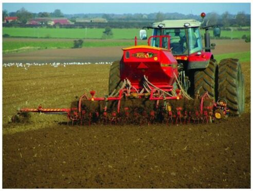 Tractor sowing spring barley in field.