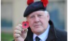 Black Watch veteran George McLuskie holds up a red artificial poppy.