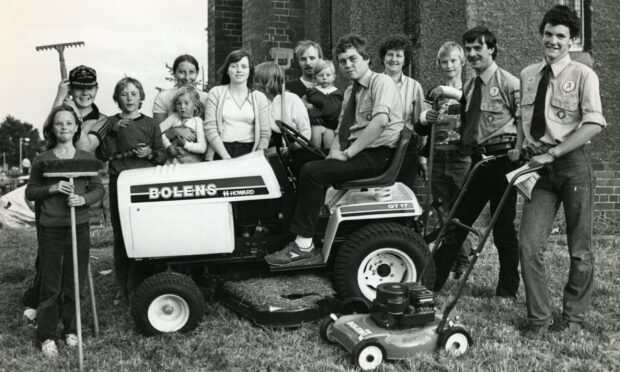 Scouts and helpers cut the grass at Mid Craigie Parish Church in 1983, after bride and groom-to-be Jean Innes and David Barclay complained about having to have photos taken in the long grass. Image: DC Thomson.