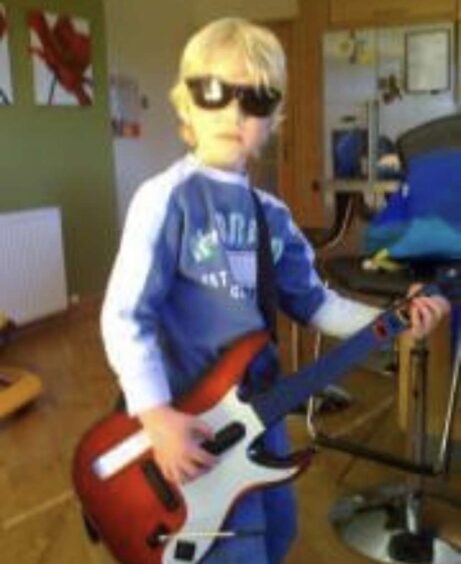 A young Ben Walker, wearing sunglasses, with a Guitar Hero guitar.