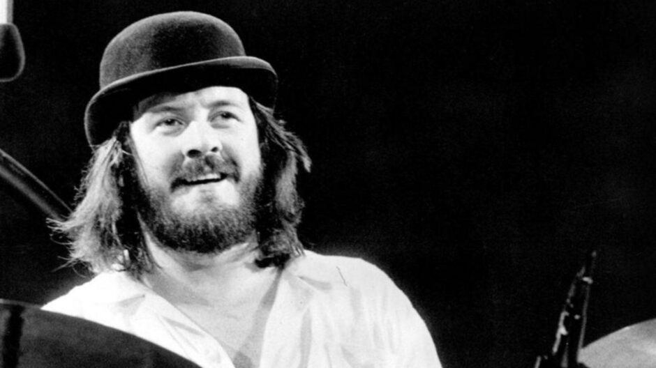 Black and white photo of Led Zeppelin drummer John Bonham wearing a bowler hat while performing. 