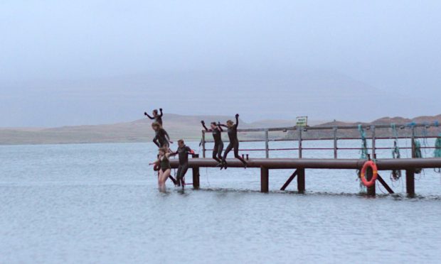 Rebecca, third from left, joins the group in jumping off the jetty despite ditching her wetsuit. Image: Stephen David Photography.