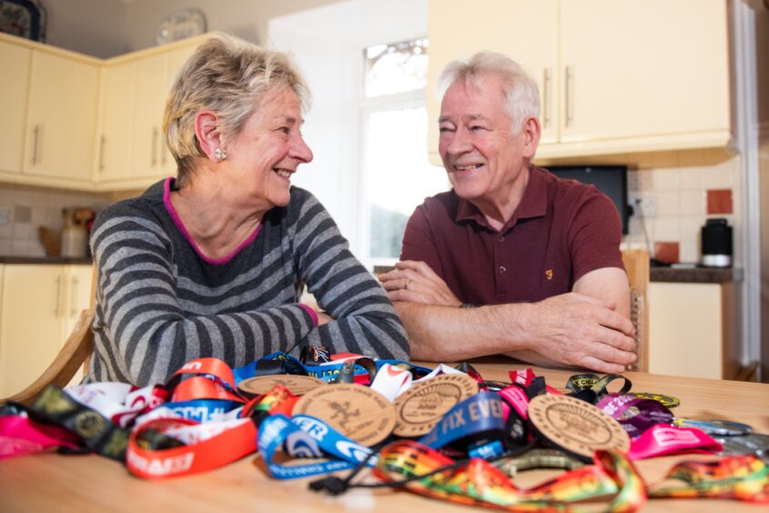 Lesley and Lawrence Richardson at their kitchen table with a pile of medals in front of them.