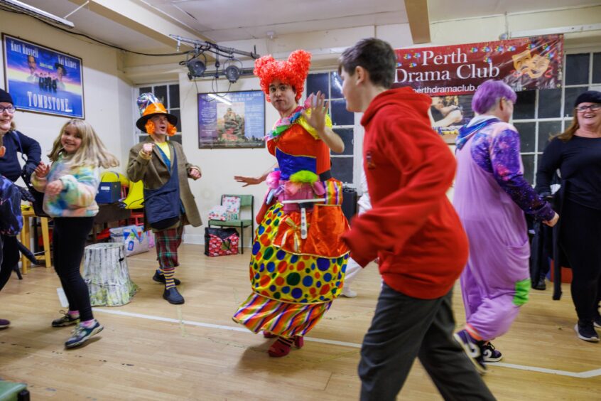 Cast members dancing around rehearsal room in colourful costumes