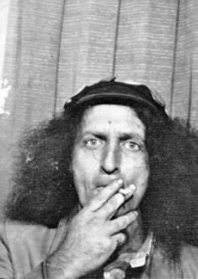 Ian Ross photobooth picture. He is smoking a roll up cigarette and has wild frizzy hair.