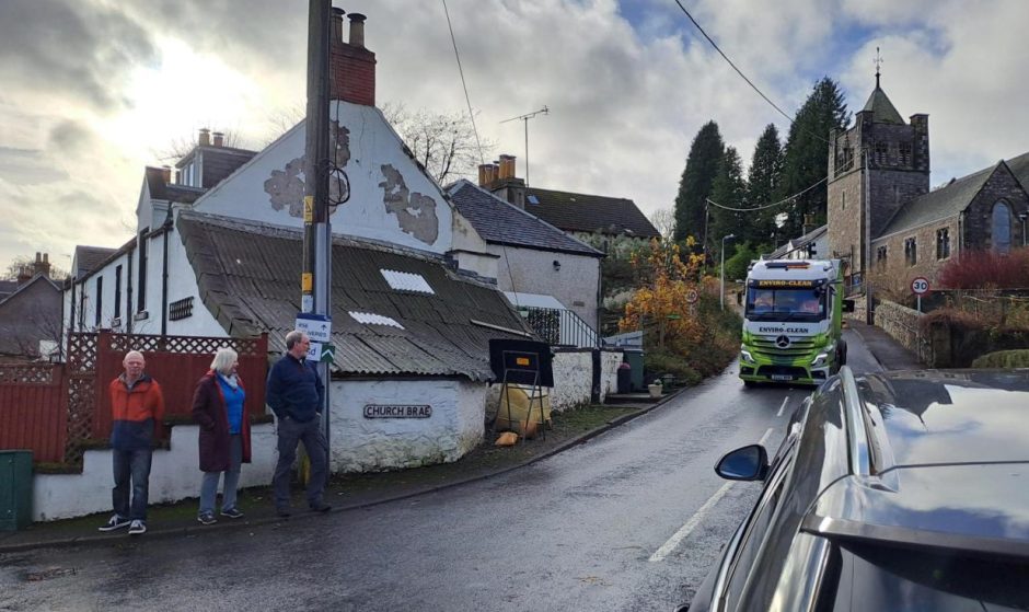 Three people standing beside a narrow road in Glenfarg while a lorry drives down it.