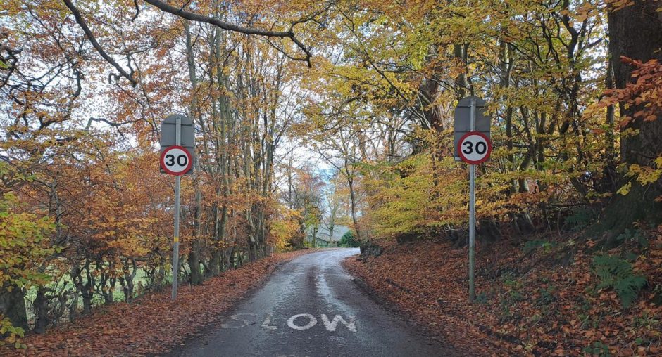 Narrow road at entrance to Glenfarg, with 30mps sign and overhanging trees.