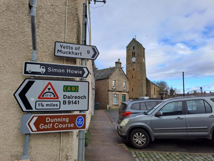 Centre of Dunning, with road sign to Simon Howie plant and St Serf's Church tower in background.