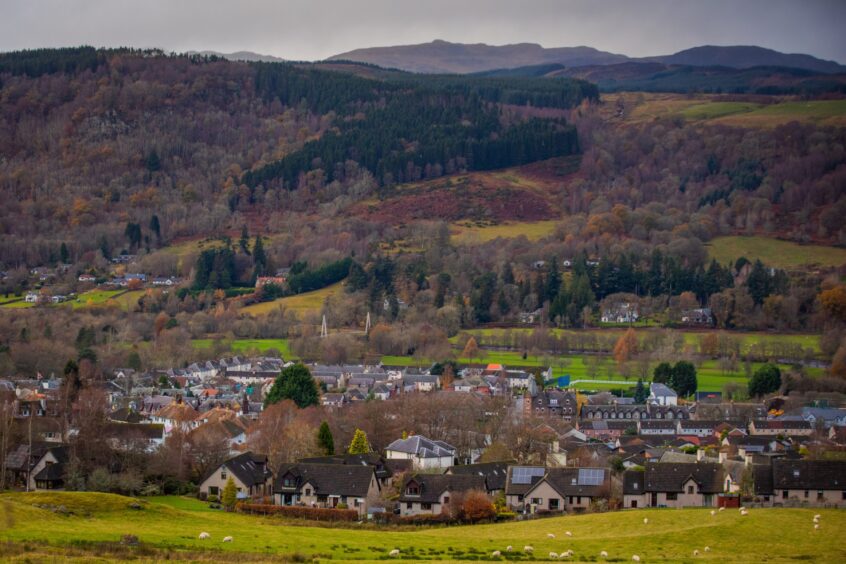 Aberfeldy nestled in countryside with autumnal trees and mountains behind.