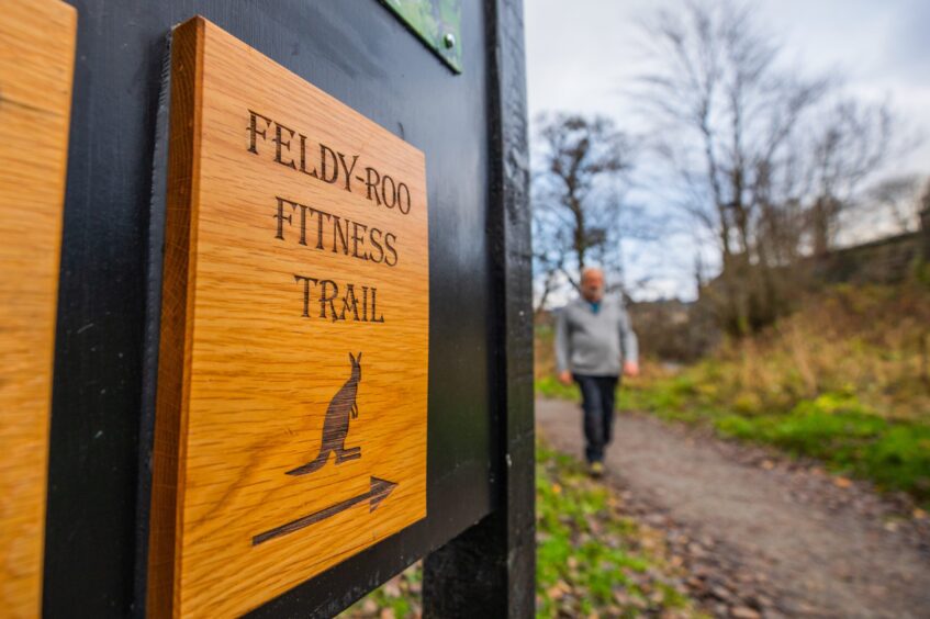man walking past wooden sign for Feldy-Roo fitness trail in Aberfeldy.
