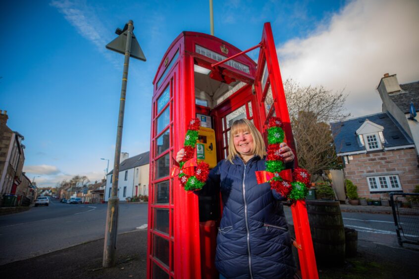 Corrina Robertson holding decorations in front of Muthill phone box