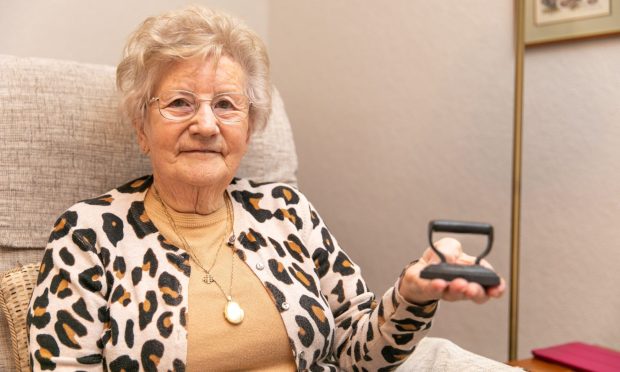 Image shows Beth Baxter holding a miniature iron that she inherited from her grandmother via her mother. Beth is aged 89 and sitting in an armchair holding the tiny iron in the palm of her hand.
